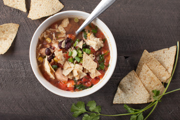 Homemade Taco Soup in small white bowl with crushed tortilla chips on dark wooden background above shot