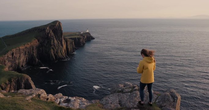 Adventure Woman taking photograph of sunset ocean view with smartphone photographing scenic landscape nature background enjoying vacation travel. Neist Point Lighthouse, Isle of Skye, Scotland