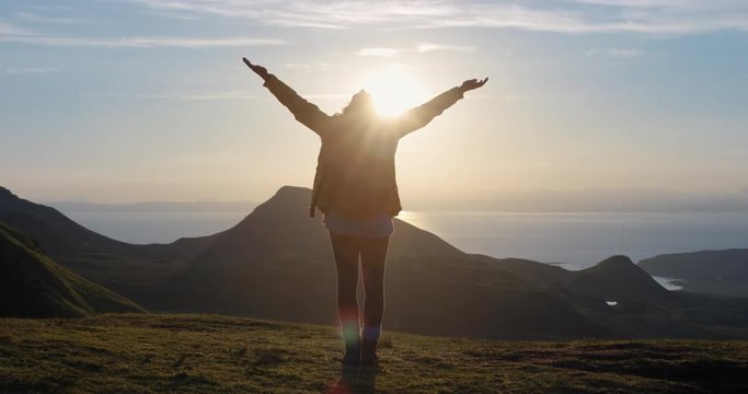 Woman with arms raised on top of mountain looking at Sunset view Hiker Girl lifting arm up celebrating life scenic nature landscape enjoying vacation travel adventure Isle of Skye Scotland