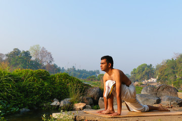 An Indian yogi performing yoga asanas on a riverbank in India.