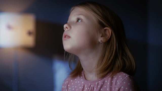 Curious Little Girl In Her Bedroom At Night, Stands On Tiptoe And Looks Out Of The Window. Shot On RED EPIC-W 8K Helium Cinema Camera.