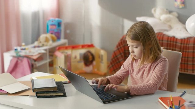Long Shot of a Cute Young Girls Typing on Laptop while Sitting at Table in Her Room. Shot on RED EPIC-W 8K Helium Cinema Camera.
