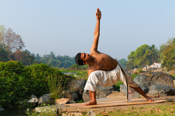 An Indian yogi performing yoga asanas on a riverbank in India.