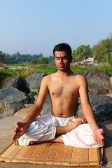 Naklejka na ściany i meble An Indian yogi meditating on a riverbank in India.