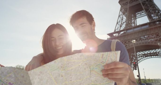 Tourist couple reading City Map under Eiffel Tower Paris planning European holiday Summer Vacation