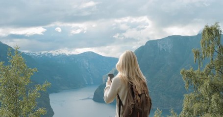 Woman taking photograph fjords with smartphone photographing scenic landscape from high up nature background view enjoying Norway vacation travel adventure