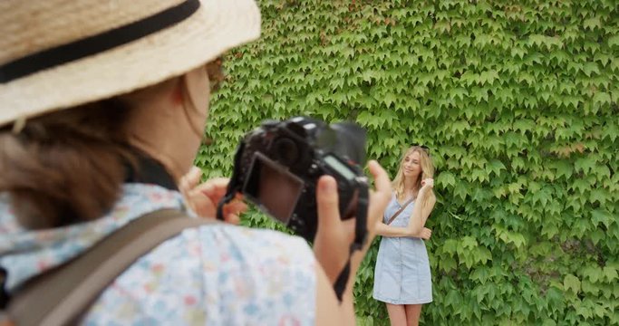 Professional photographer taking photo of model woman posing in front green wall of plants vertical garden girls enjoying European summer holiday travel vacation adventure