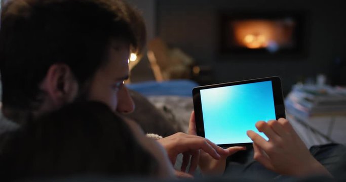 Closeup of couple using digital tablet by fireplace viewing travel photos on touchscreen browsing social media sharing wanderlust inspiration on digital device