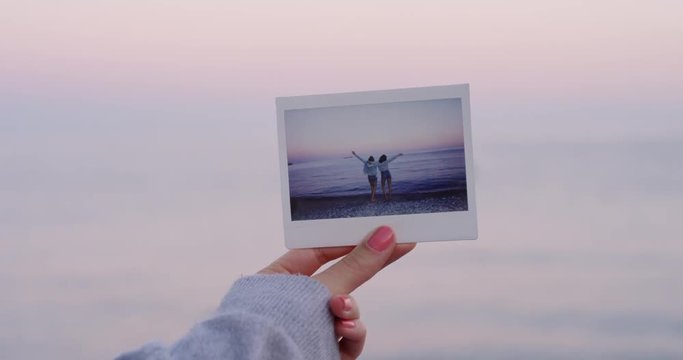 Hand holding instant photo on tropical beach at sunset