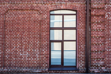 Urban design. Brick wall of an old house with a window. Reflection of a house in a window of red brick.