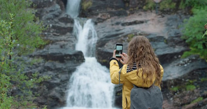 Woman hiker taking photo of waterfall smartphone photographing scenic landscape nature background view enjoying vacation travel adventure