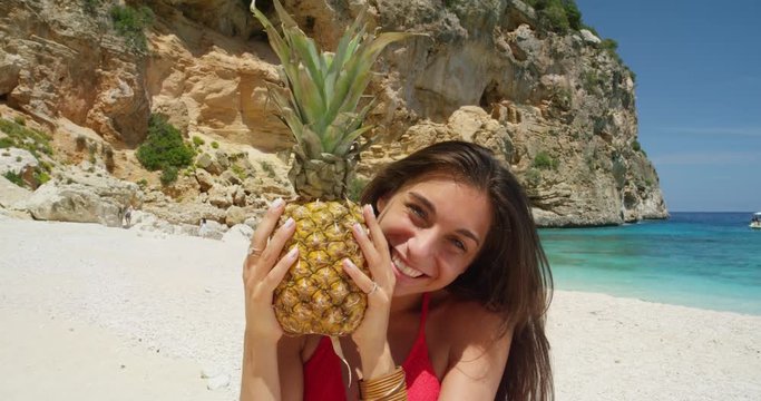 Happy woman holding pineapple posing for camera being silly and playful on tropical beach summer vacation holiday