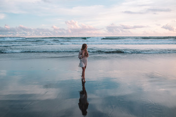 Blonde hair girl stands on the beach during sunset in Indian ocean, Bali, Indonesia