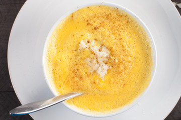 Roasted Butternut Squash Soup with shaved Parmigiano Reggiano Cheese and cinnamon on a dark wooden background on a white plate top view