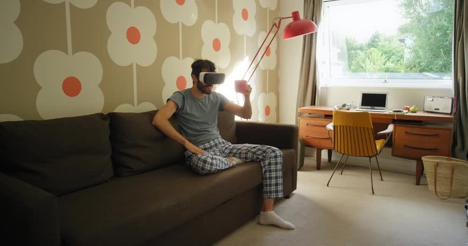 Young man wearing virtual reality headset having video chat sitting on sofa at home watching 360 video imagination concept retro styled modern apartment