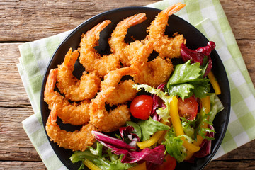 Shrimp in a breaded and salad of fresh vegetables close-up on a plate. horizontal top view 