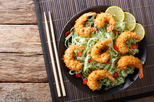 Shrimp tempura with green pasta and sesame close-up on a plate. horizontal top view