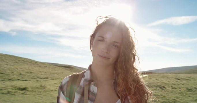 Close up portrait of Beautiful Young Woman Smiling in nature with hair blowing in wind Hiker Girl standing in front of sun flare trekking in Scotland Slow Motion