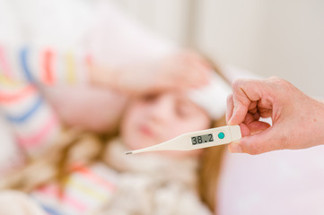Sick kid with high fever lying in bed and mother taking temperature