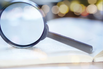 Close-up of a magnifying glass standing on an open book with bokeh light background