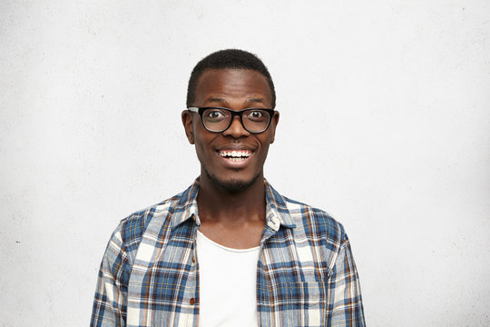 Portrait of happy bug-eyed young African college student in black glasses looking at camera with wide smile of excitement and surprise showing white straight teeth. Human emotions and feelings