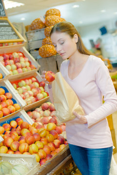 Lady in greengrocers putting nectarine into paper bag