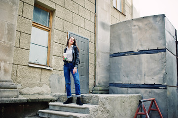 Portrait of stylish young girl wear on leather jacket and ripped jeans with cup of coffee. Street fashion model style.