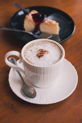 A cup of cappuccino coffee with cake on wooden table background with vintage filter