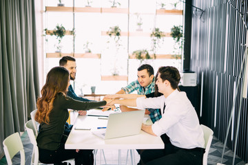 Young businesspeople putting hands together on the table at the office meeting