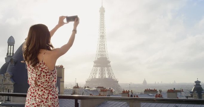 Tourist couple taking photograph of Eiffel Tower using smartphone from hotel balcony at sunrise photographing scenic Paris cityscape background view enjoying European honeymoon vacation travel adventure