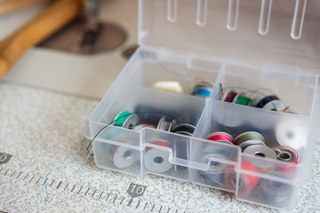 The place of work of the dressmaker. Many bobbins for sewing in a box on the desktop. Multi-colored...