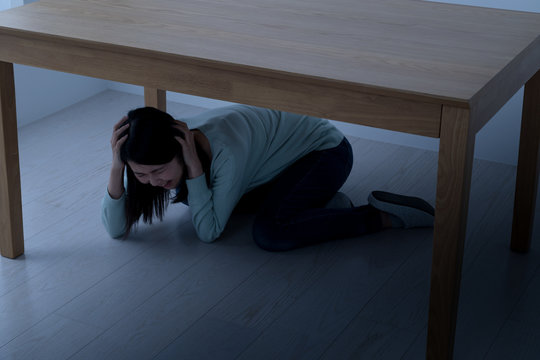 テーブルの下に隠れる女性、地震、震災、災害