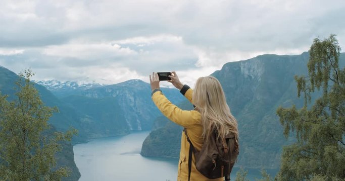 Woman taking photograph fjords with smartphone photographing scenic landscape from high up nature background view enjoying Norway vacation travel adventure