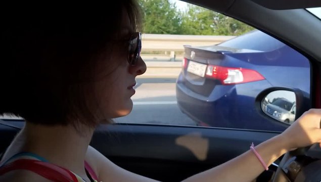 Young woman driving car and waiting in traffic jam on highway at summer day