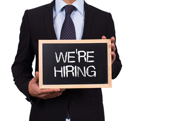 Businessman holding mini blackboard with WE'RE HIRING message