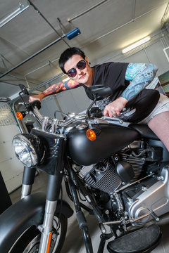 Cool sensual biker girl sitting on old fashioned motorcycle in garage interior on grey wooden wall background, vertical picture