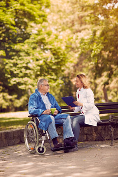 nurse talking with patient in wheelchair checking up the history of the disease outdoor.
