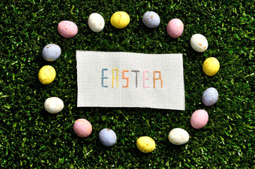 Easter cross stitched on textile isolated on artificial grass displayed with speckled eggs