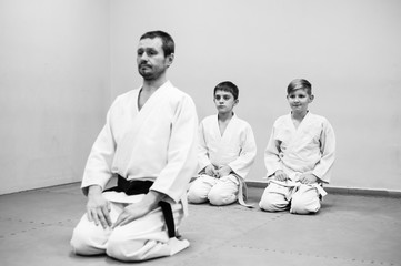 Children in a kimono sit on the tatami with a coach at a seminar on martial arts.