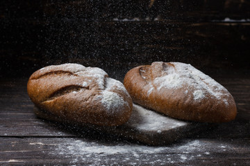 Two black bread with flour on a wooden background. Advertising bread. Leaning flour.