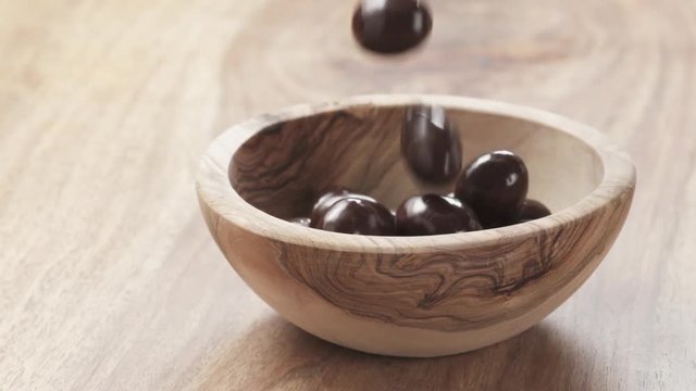 Slow motion of almonds covered with chocolate fall in wood bowl on wooden table, 180fps prores footage