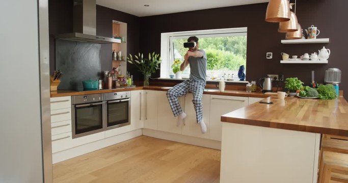 Happy young man wearing virtual reality headset dancing in kitchen wearing pajamas in the morning listening to music 360 video imagination concept