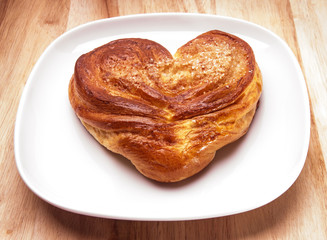 Yeast sweet buns in the shape of a heart  on a dish on an wooden table.