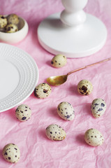 Table setting with white plate, golden spoon, green twig and quail eggs on a pink tissue paper....