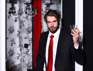 bearded man, businessman in suit, red tie holds whiskey glass