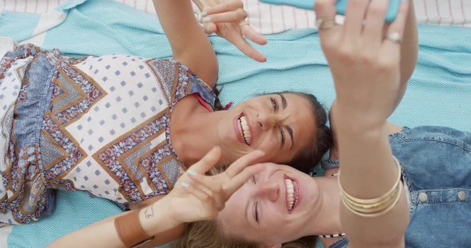 Top view of teenage girl friends taking selfie photo with smart phone lying on back sticking out tongue smiling laughing at beach direct from above