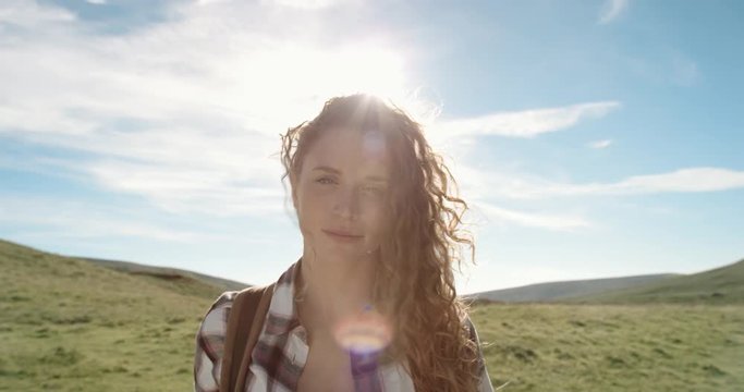 Close up portrait of Beautiful Young Woman Smiling in nature with hair blowing in wind Hiker Girl standing in front of sun flare trekking in Scotland Slow Motion