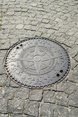 Fototapeta na wymiar manhole with wind rose on the stone pavement