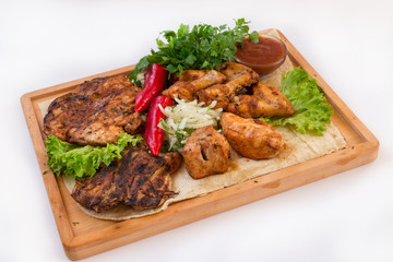 Meat dish. Pieces of roasted meat, parsley, sauce, red pepper, lettuce leaves lie on a wooden board. Isolated on white background