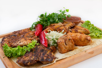 Meat dish. Pieces of roasted meat, parsley, sauce, red pepper, lettuce leaves lie on a wooden board. Isolated on white background